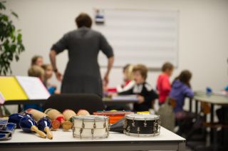 Nascholing muziek - Muziekinstrumenten met op de achtergrond een lerares die lesgeeft aan wat kinderen